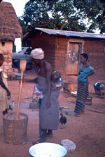 47. Mother pounding corn while her baby sleeps on her back